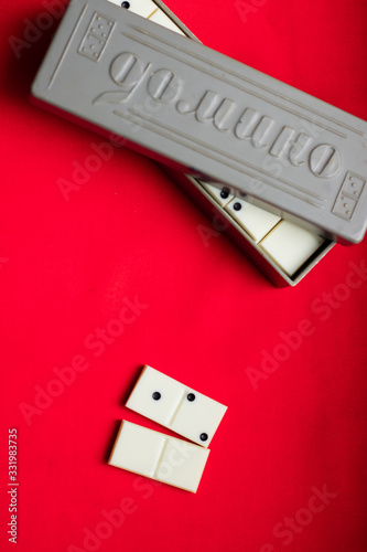 Two domino bones lie next to a gray box on a red fabric background. Plenty of room for text.On the bump of the case there is an inscription “Domino”