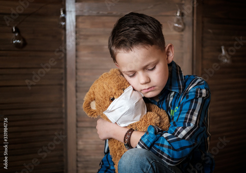 a cute European boy is holding a Teddy bear in a medical mask. concept of quarantine during the covid-19 pandemic