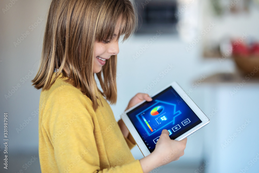 Little girl using a domotic system with her digital tablet while standing at home. Little girl using a domotic system with her digital tablet while standing at home.