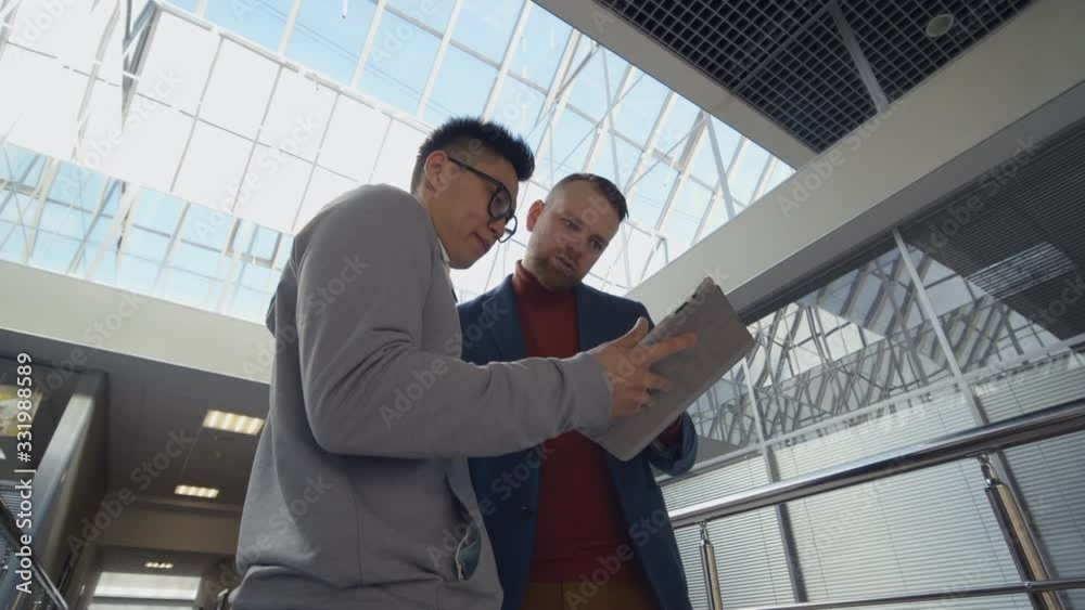 Diverse business colleagues reading report on tablet pc in corridor Diverse business colleagues reading report on tablet pc in corridor