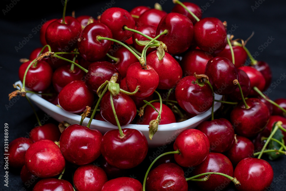 Red cherries on black background coming out and hanging from the plate Red cherries on black background coming out and hanging from the plate