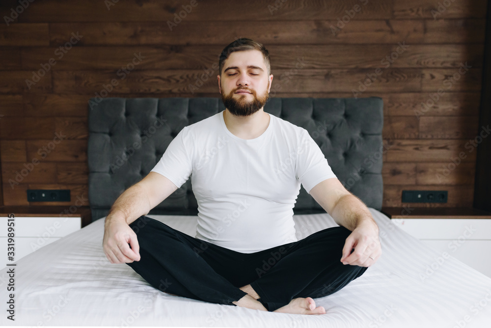 Fototapeta premium Handsome caucasian man meditating and mindful on his bed in bedroom