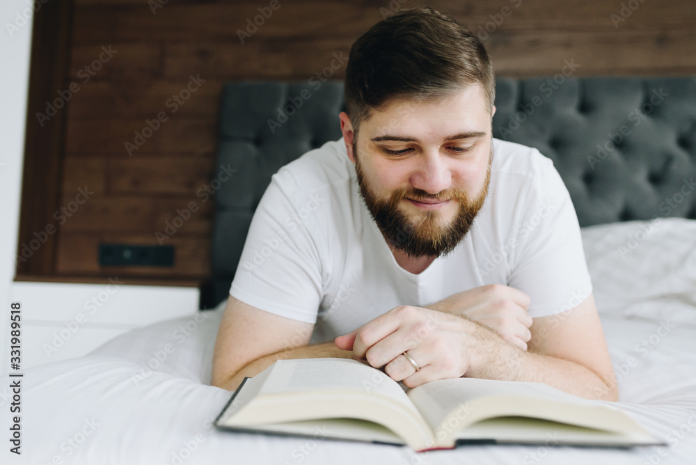 Close up young handsome caucasian man reading a book in bed during the quarantine Close up young handsome caucasian man reading a book in bed during the quarantine