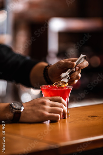 Expert barman making a hot red cocktail at a bar. Red alcoholic drink in glass