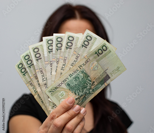 close up of one banknote with a face value of PLN 100 Polish money, zloty held  in the hands of a women on a grey background