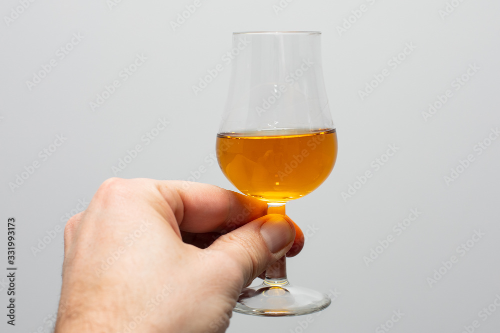 close-up of  whiskey tasting glass with whiskey held in a hand on a gray background