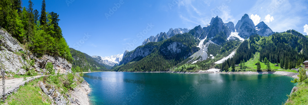 Famous Lake Gosau and Gosaukamm with Mount Dachstein. Spring is here! The snow is melting and spring brings the luscious green back to nature.  The sun is about to hide behind the high peaks.