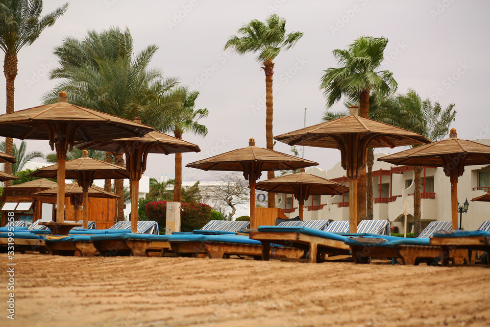 Empty tropical sandy beach with wooden umbrellas and blue sun beds Empty tropical sandy beach with wooden umbrellas and blue sun beds