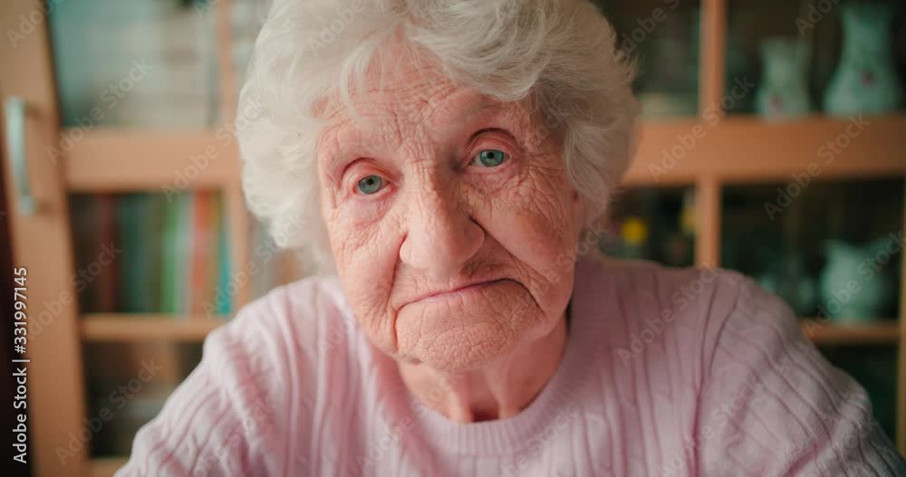 Close-up face of a sad old woman with deep wrinkles winking her eyes.