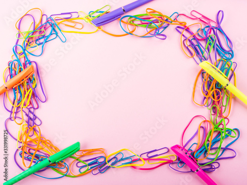 Colorful rubber bands, pens and clips frame on pink paper background. Flat lay