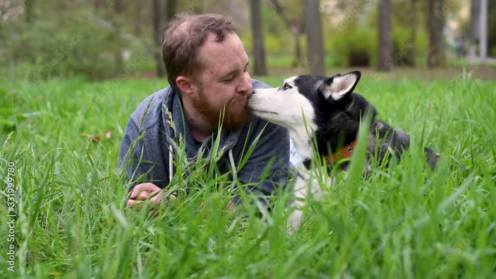 Dog and man with beard are lying in grass Dog and man with beard are lying in grass