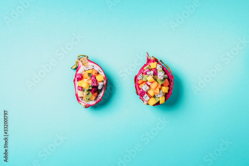 Exotic fruit salad served in half of dragon fruit on blue background. Copy space. Tropical travel, exotic fruit. Vegan and vegetarian concept.
