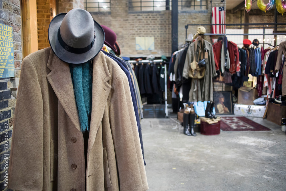 Spitalfields flea market. Woolen cashmere men's coat with felt hat on the background of rows with clothes for sale