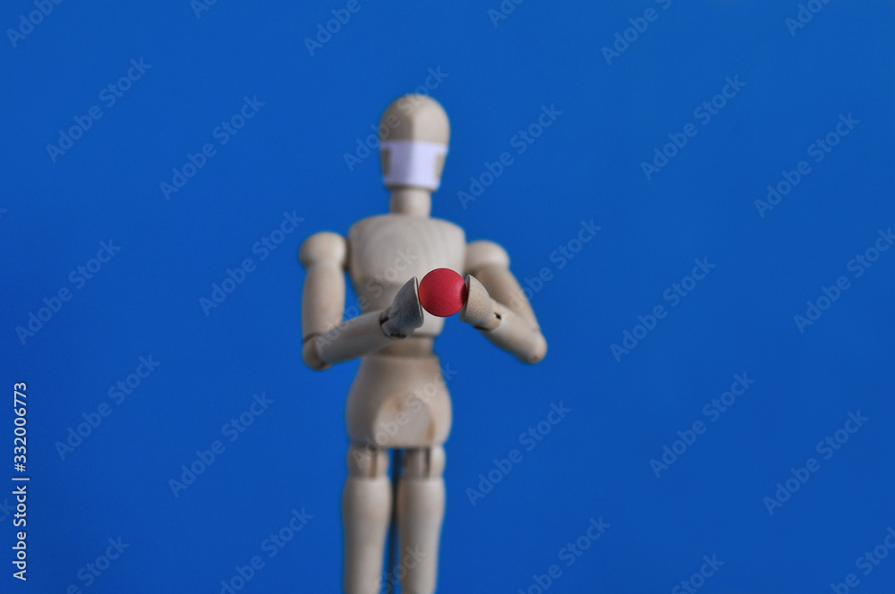 Wooden figure of a mannequin in a medical mask holding a red pill on a blue background. Coronavirus, pandemic and epidemic concept Wooden figure of a mannequin in a medical mask holding a red pill on a blue background. Coronavirus, pandemic and epidemic concept