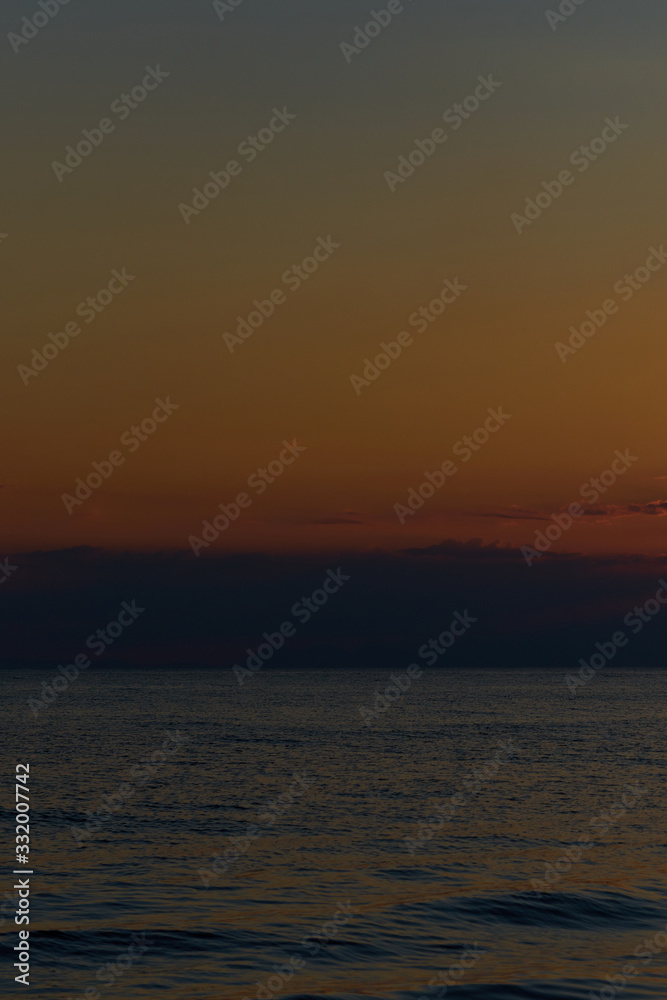 Sunset at the tropical beach, sun behind clouds reflects on water.