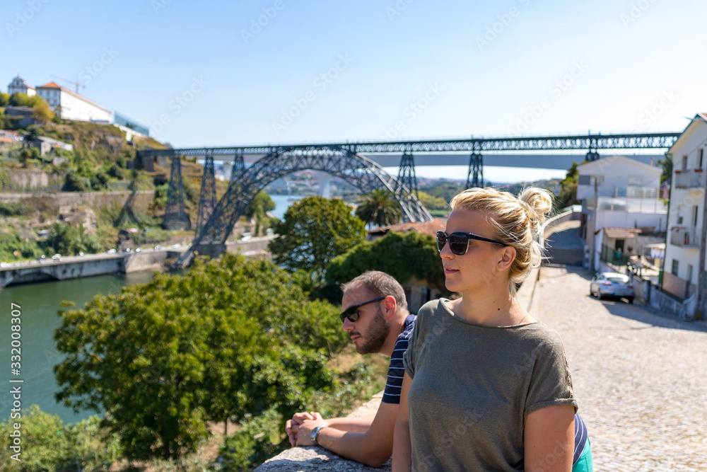 Tourist couple with sunglasses on posing for a photo in front of an arch bridge Maria Pia in Porto