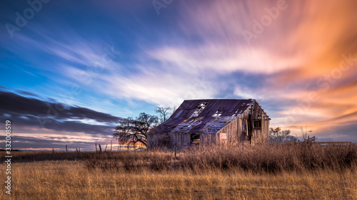 Old rural farmhouse in the countryside during a very colorful sunset. There is a grass meadow and a few trees. © Scott Book