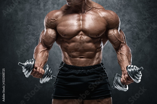 Muscular man working out with dumbbells, isolated on wall background. Strong male naked torso abs photo