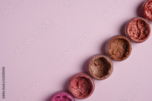 Shades of different lipsticks in round jars stand diagonally on a pastel lilac background in the right corner of the frame