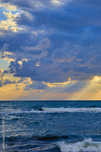 Colorful sunset at the tropical sandy beach  sun behind the clouds and waves with foam hitting sand.