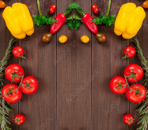 Vegetable frame with place for text: cherry tomatoes, peppers, rosemary and parsley leaves. Fresh vegetables on wooden background
