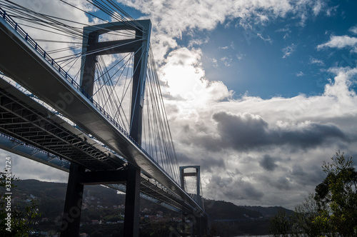 Suspension bridge with sun behind clouds photo