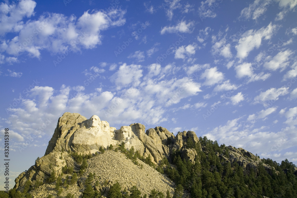 White puffy clouds behind Presidents George Washington, Thomas Jefferson, Teddy Roosevelt and Abraham Lincoln at Mount Rushmore National Memorial, South Dakota