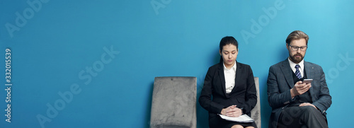 Two male and female business people waiting in line to be called into job interview at office
