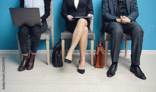Three impersonalized businesspeople sitting on chairs busy with their stuff waiting for colloquy