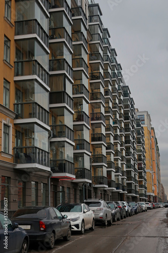 cars parked along the facade of a modern residential complex with glass balconies © Sergey