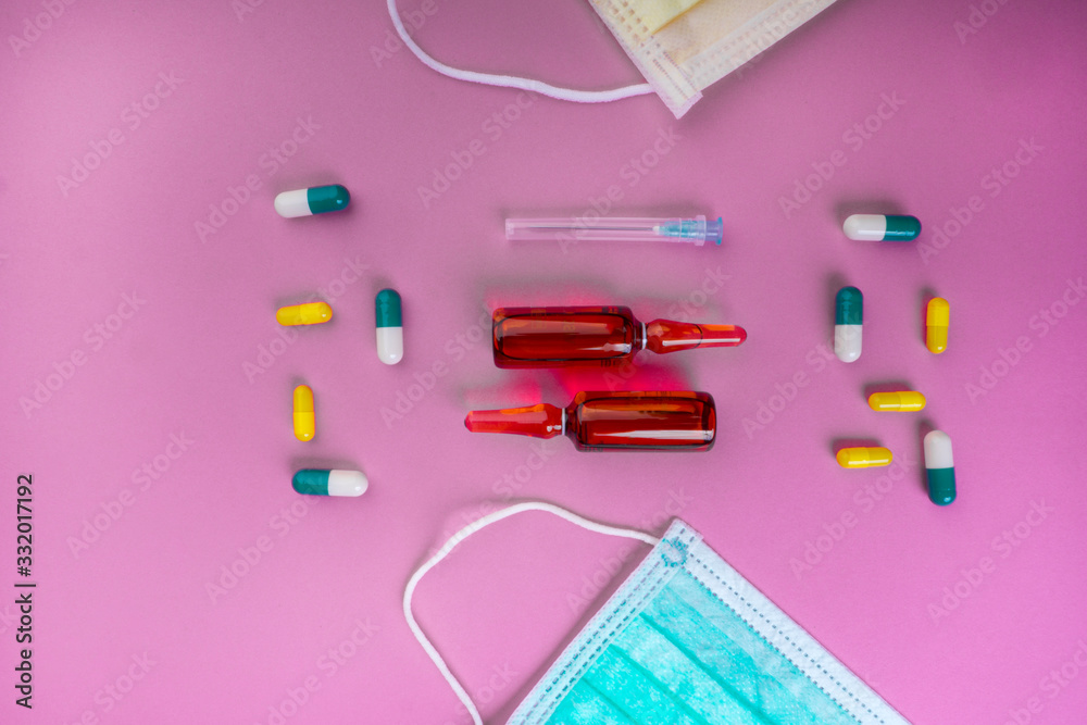 Protective face mask on pink background, pills, needle