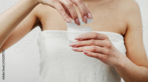 Midsection of lady wrapped in white bath towel opening plastic cream jar, focus on hands and box