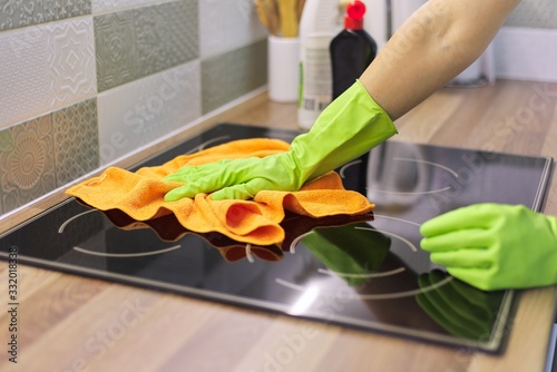Woman hand in gloves polishing hob glass with microfiber cloth photo