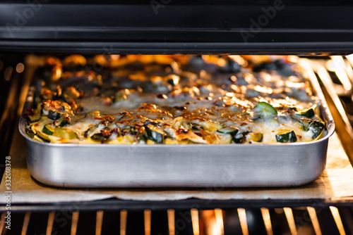 Close-up of a traditional lasagna made with zucchini and bacon in a baking tray in oven