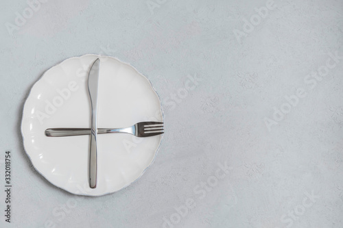 Fasting and diet concept. Empty white plate with fork and knife on neutral concrete kitchen table. Top view with copy space