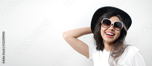 Portrait of young grinning brunette wearing sunglasses and black hat, isolated on white background