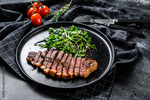 Sliced sirloin steak, marbled beef meat with arugula. Black background. Top view