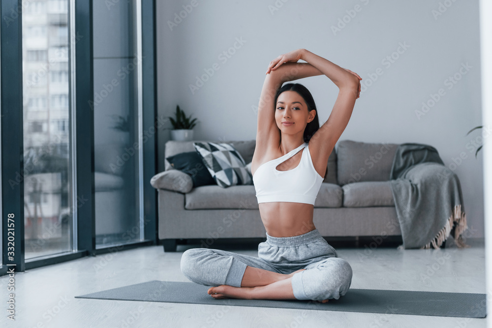 Obraz premium Does yoga exercises. Young woman with slim body shape in sportswear have fitness day indoors at home