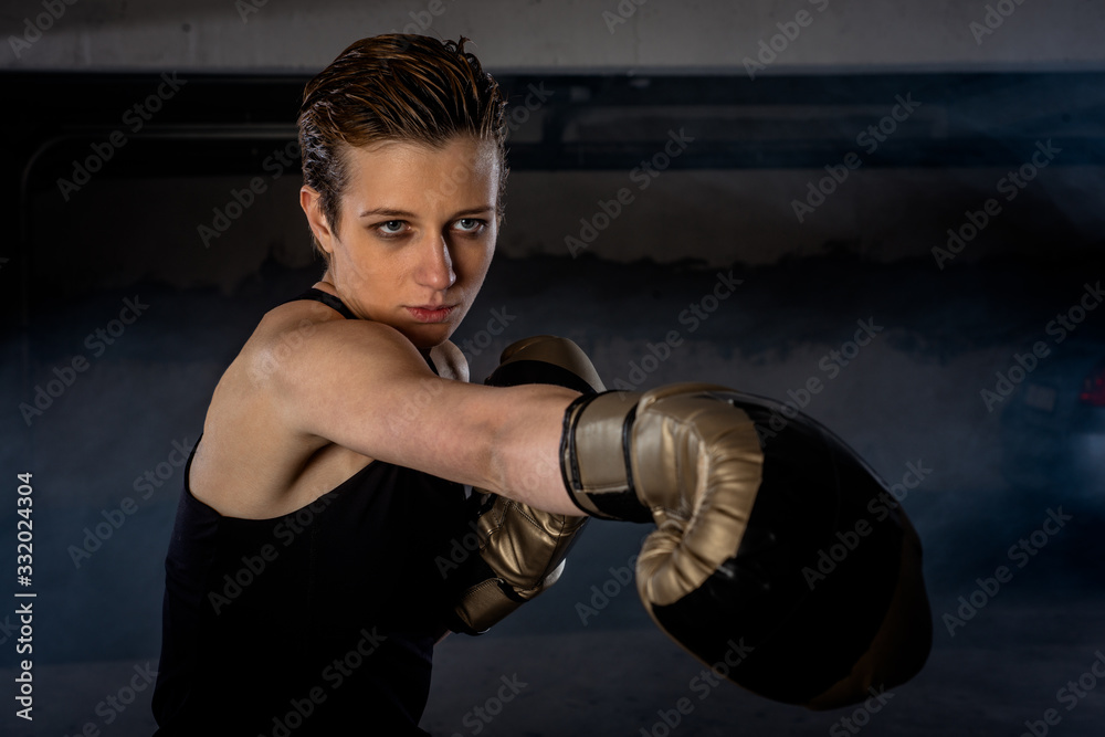 Closeup picture of beautiful female boxer practicing her punches with gold boxing gloves