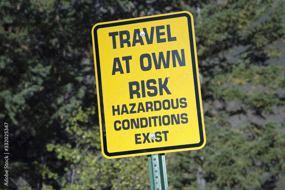 Yellow warning sign reading Travel At your own Risk alerting travelers that hazardous conditions exist