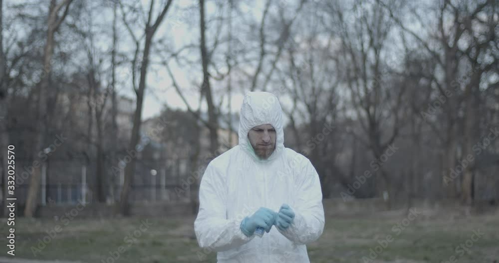 Portrait of male scientist in protective suit removes his gloves and desinfects hands while standing in urban daytime park during pandemic coronavirus quarantine time 4K Portrait of male scientist in protective suit removes his gloves and desinfects hands while standing in urban daytime park during pandemic coronavirus quarantine time 4K