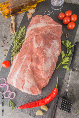 Boston butt - a large raw piece of meat on a black slate with spices and a hammer for beating meat, top view.