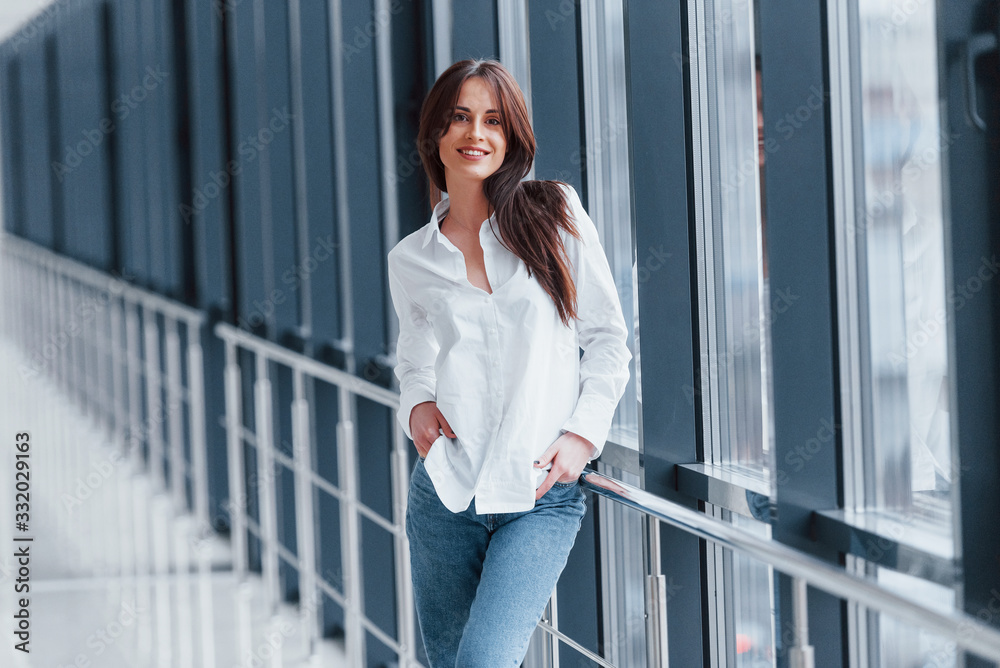 Brunette in white shirt leaning on railings indoors in modern airport or hallway at daytime Brunette in white shirt leaning on railings indoors in modern airport or hallway at daytime