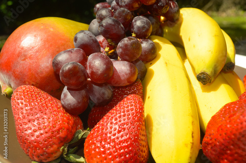 Tropical fruits as banana mango strawberries red grapes  in a brown plate garden picture image background