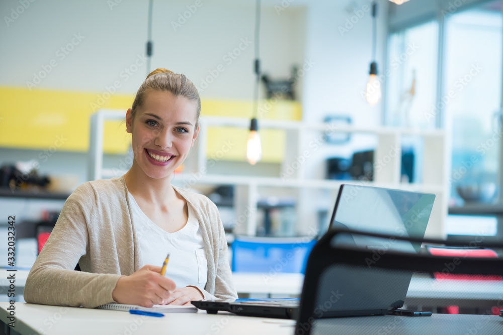 Obraz premium Young female business woman using laptopat her work and staying alone after work to finish her job, looking and smiling into camera.
