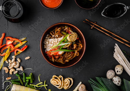 Chinese dishes in a clay plate on a black concrete background with ingredients for delivery