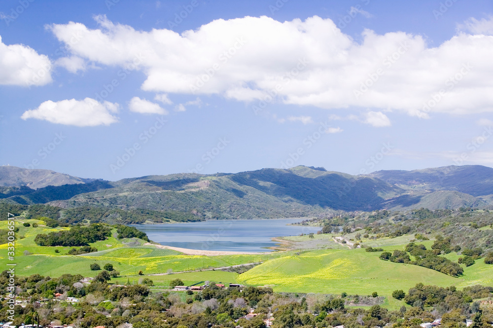 Elevated view of Lake Casitas and green fields in spring with white puffy clouds, shot from Oak View, near Ojai, California