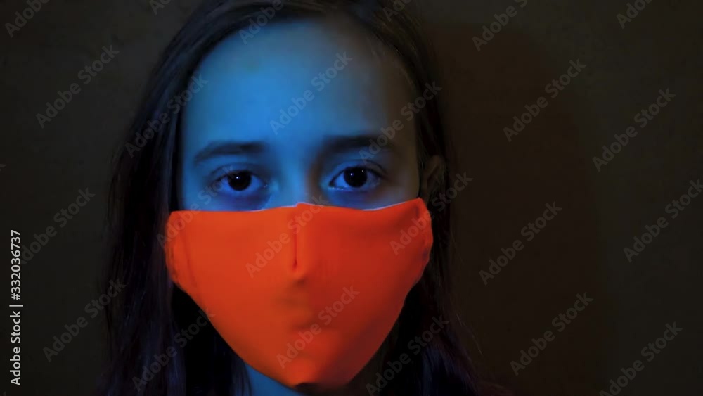 A teenager on a background of flashing lights of a siren. Coronavirus and Flu epidemic concept. Girl, standing in the dark in a mask, blinks and looks around. A teenager on a background of flashing lights of a siren. Coronavirus and Flu epidemic concept. Girl, standing in the dark in a mask, blinks and looks around.