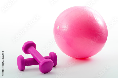 Strength increase through weightlifting and aerobic exercise and muscle toning exercising concept inflatable fitness ball and pink weights isolated on white background
