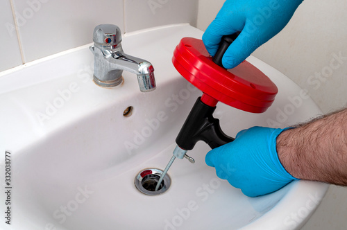 Plumbing issues, occupation in sanitation and handyman contractor concept with plumber repairing drain with plumbers snake (steel spiral that twists through pipes to collect dirt) in residential sink
